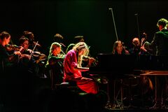 Een vrouwelijke pianist speelt op een vleugelpiano, omringd door een orkest in een sfeervolle, donkere setting.
