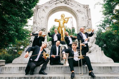 Groep muzikanten in formele kleding poseert voor een gouden standbeeld in een park.