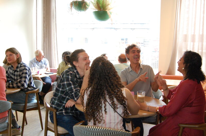 Groep vrienden die lachen en met elkaar praten aan een ronde tafel in een sfeervol café.
