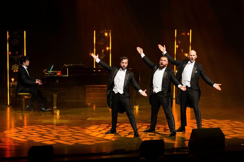 Drie mannen in smoking voeren een muzikale act op terwijl een pianist hen begeleidt.