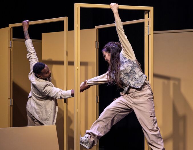 Twee performers bewegen acrobatisch aan gele deuromlijstingen op een toneel.