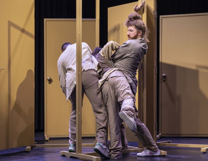 Drie performers bewegen verstrengeld tussen vrijstaande gele deuromlijstingen op een toneel.