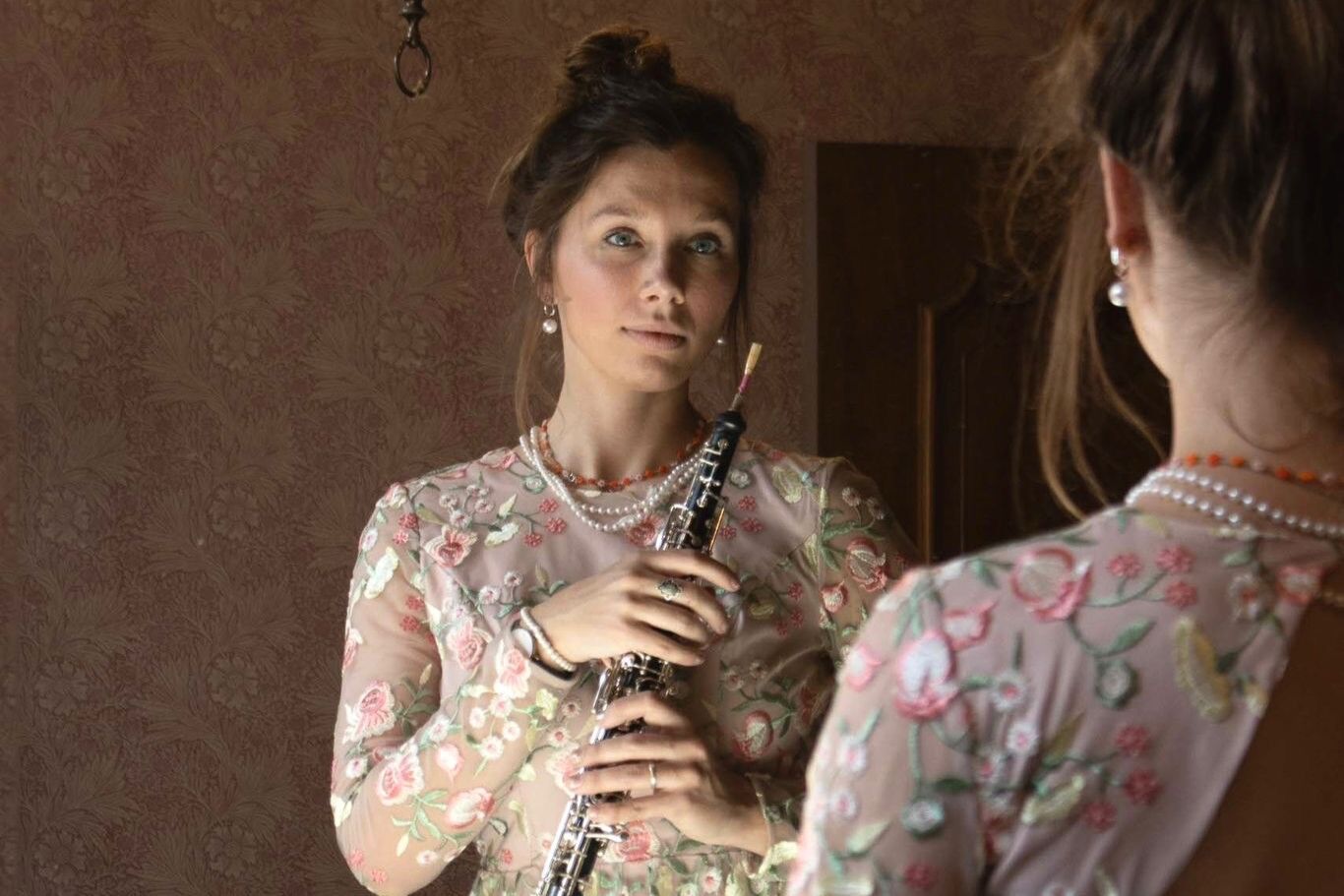 Een vrouw in een doorzichtige blouse kijkt in de spiegel terwijl ze een blokfluit vasthoudt.