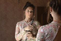 Een vrouw in een doorzichtige blouse kijkt in de spiegel terwijl ze een blokfluit vasthoudt.