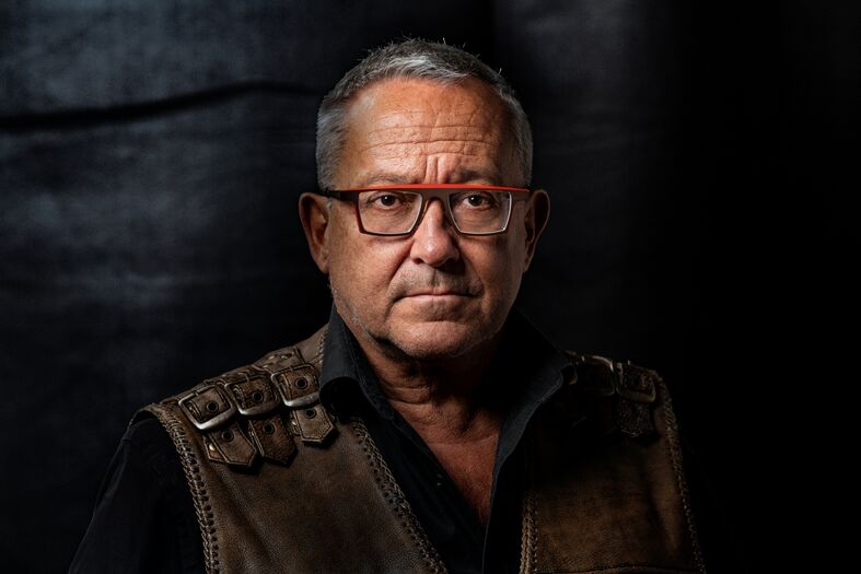 Portret foto van Tom Lanoye voor een donkere achtergrond.