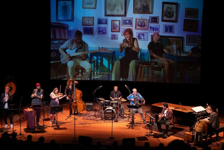 Een live band speelt op het podium met een projector die beelden van de muzikanten toont. 