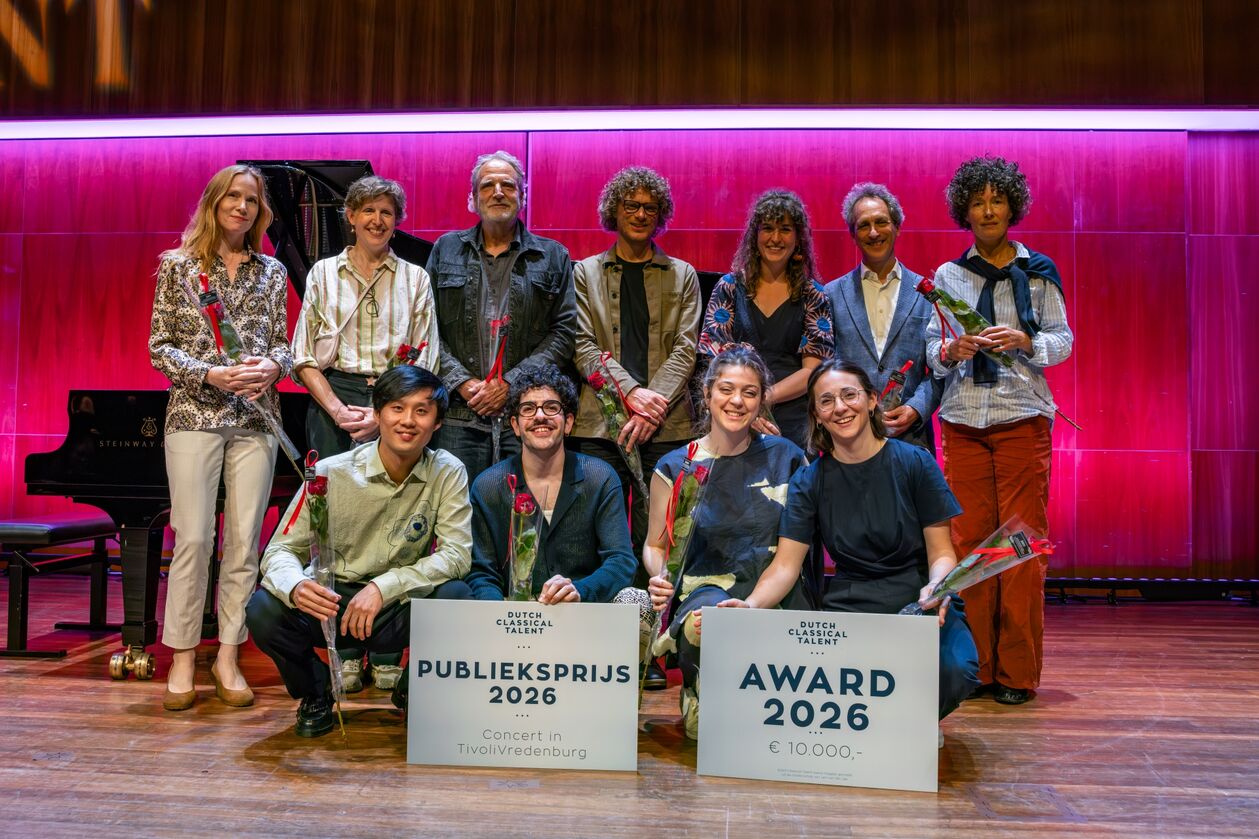 Groep van twaalf personen poseert op een podium met piano, houdend award-borden voor de Publieksprijs 2020.