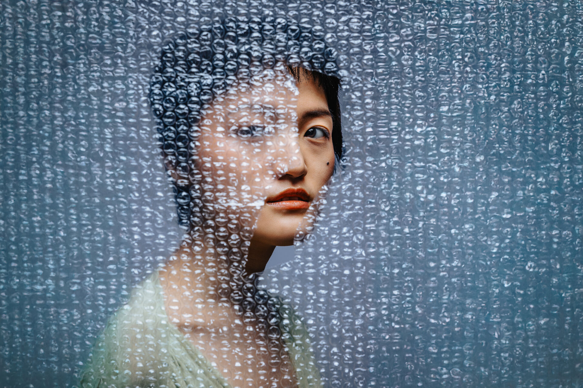 Gezicht deels zichtbaar achter doorzichtige noppenfolie met kleine ronde luchtbellen.