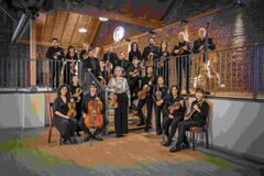 Een orkest bestaande uit 18 muzikanten, poserend op een trap met verschillende instrumenten in een sfeervolle ruimte.