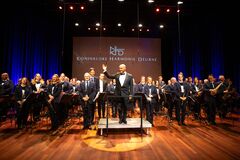 Groot orkest op een verlicht podium terwijl de dirigent het publiek groet