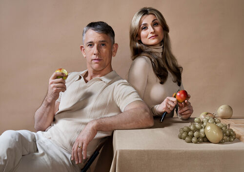 Waldemar Torenstra & Judith Noyons lichtgekleurde kleding zitten aan een tafel en houden fruit vast, met druiven en ander fruit op het tafelkleed.