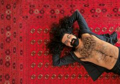 Persoon ligt op rood tapijt met armen achter hoofd en open overhemd, haar uitgespreid.