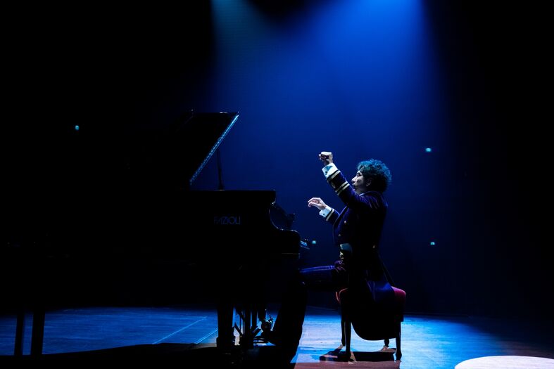 Pianist in een donker podiumlicht, terwijl hij intensief speelt en zich uitdrukt met zijn handen.