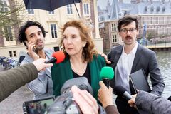 Drie personen lopen buiten langs het Binnenhof terwijl meerdere microfoons naar hen worden uitgestoken.