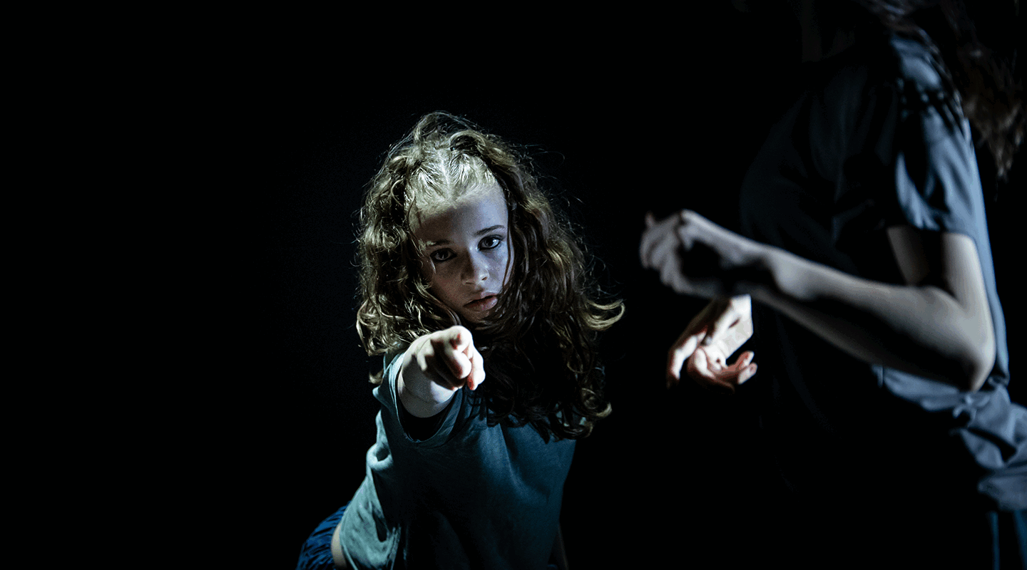 Twee dansers in een donkere omgeving; een danseres wijst met intense blik naar de camera.