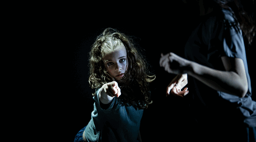 Twee dansers in een donkere omgeving; een danseres wijst met intense blik naar de camera.