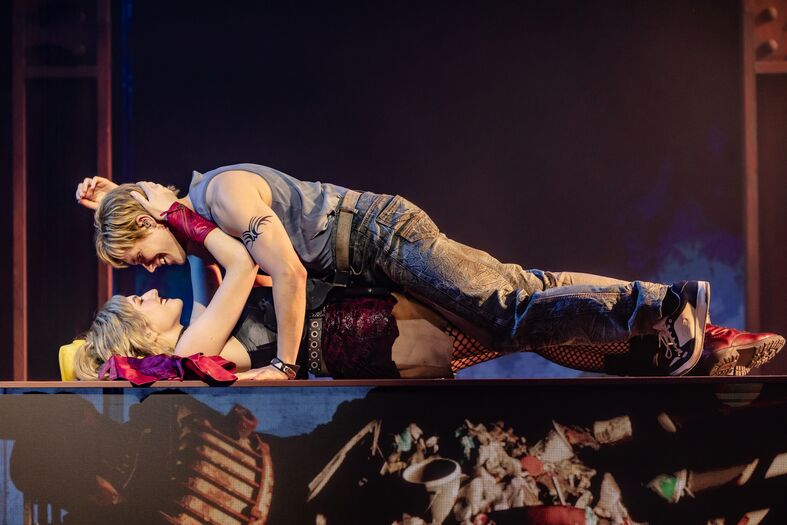 Twee acteurs in theaterkostuums voeren een passievol duet uit op een podium met theatrale belichting.