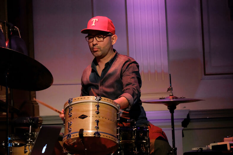 Een man met een pet speelt op een drumstel tijdens een muziekoptreden.