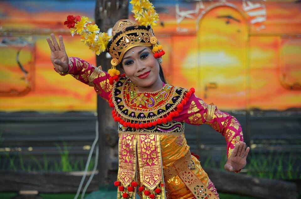 Jongevrouw in traditionele kleding danst met folkloristische elementen voor een kleurrijke achtergrond.