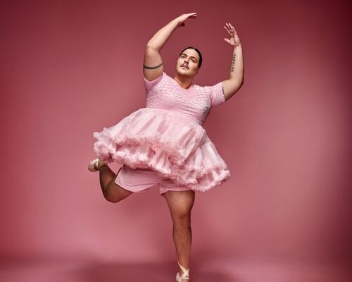 Persoon (Fimme Bakker) in roze tutu en balletpakje staat op spitzen met één been opgetild en armen gebogen boven het hoofd tegen een roze achtergrond.